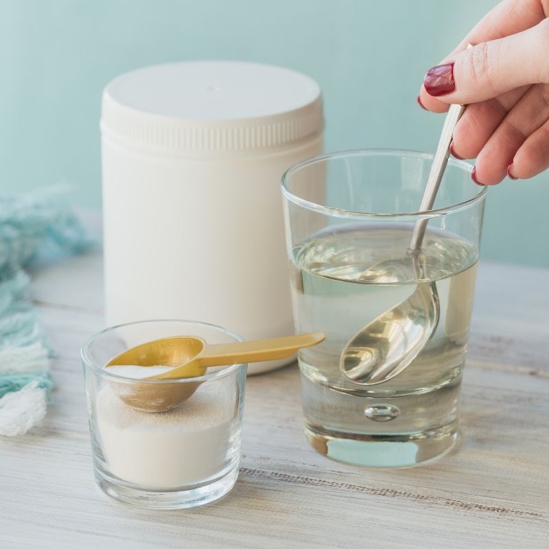 Glass of hydrolysed Collagen powder in water with a spoon and container for Collagen Powder FAQs