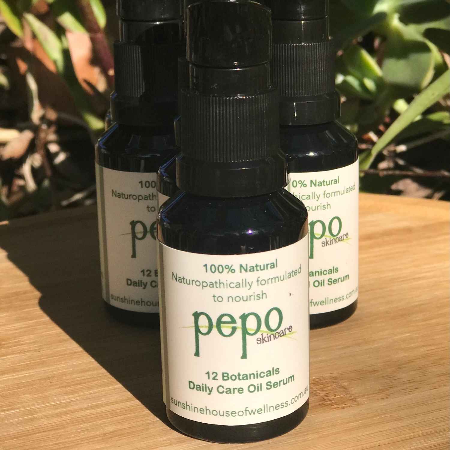Three bottles of pepo natural skincare oil serum on a wooden surface with plants in the background.