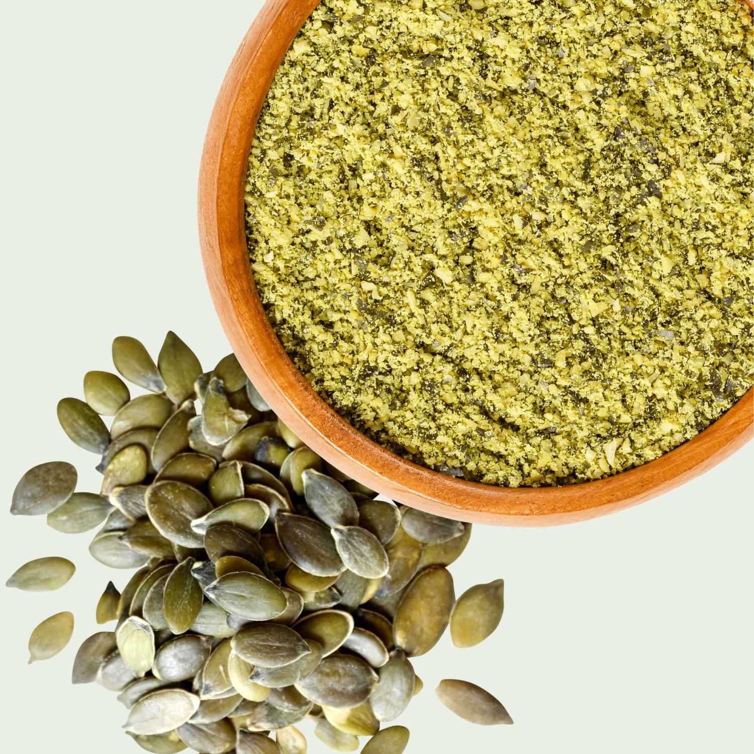 Wooden bowl filled with ground Australian pumpkin seed meal and Styrian pumpkin seeds on a light background.