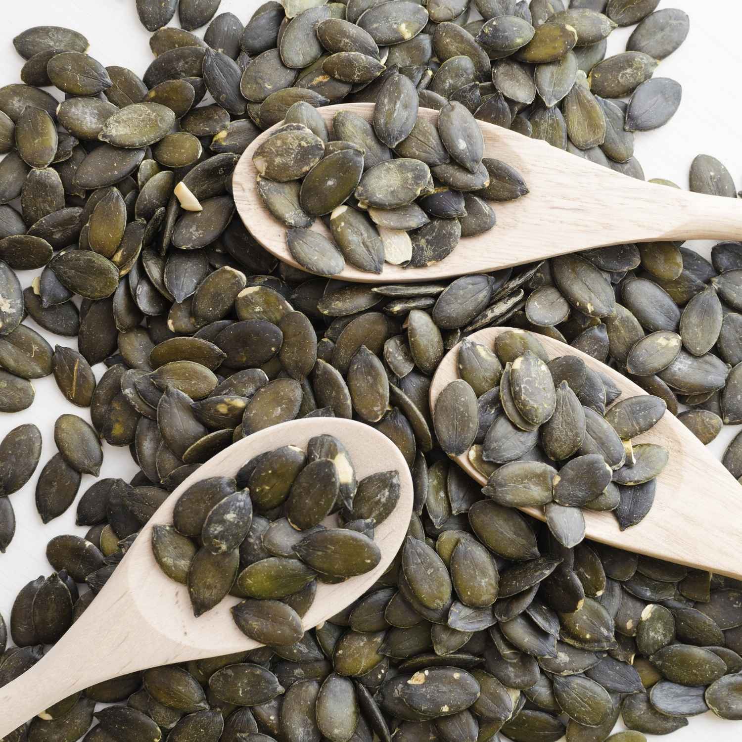 Dark green Australian Pumpkin seeds with wooden spoons on a white background