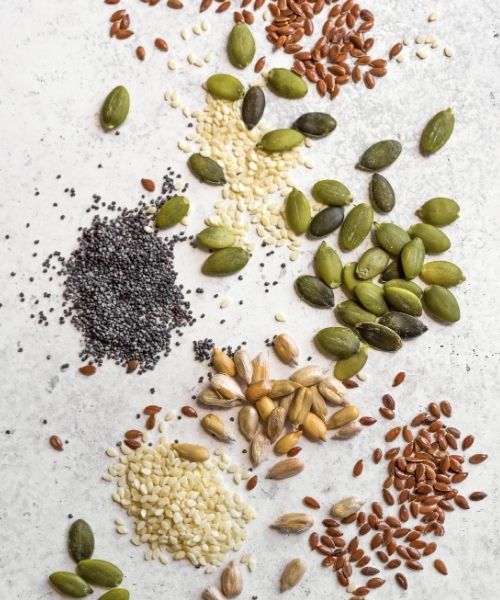 Seed cycling for hormone balance with Women's Health Naturopath Australia using sesame, pumpkin, sunflower, and flax seeds on a light background