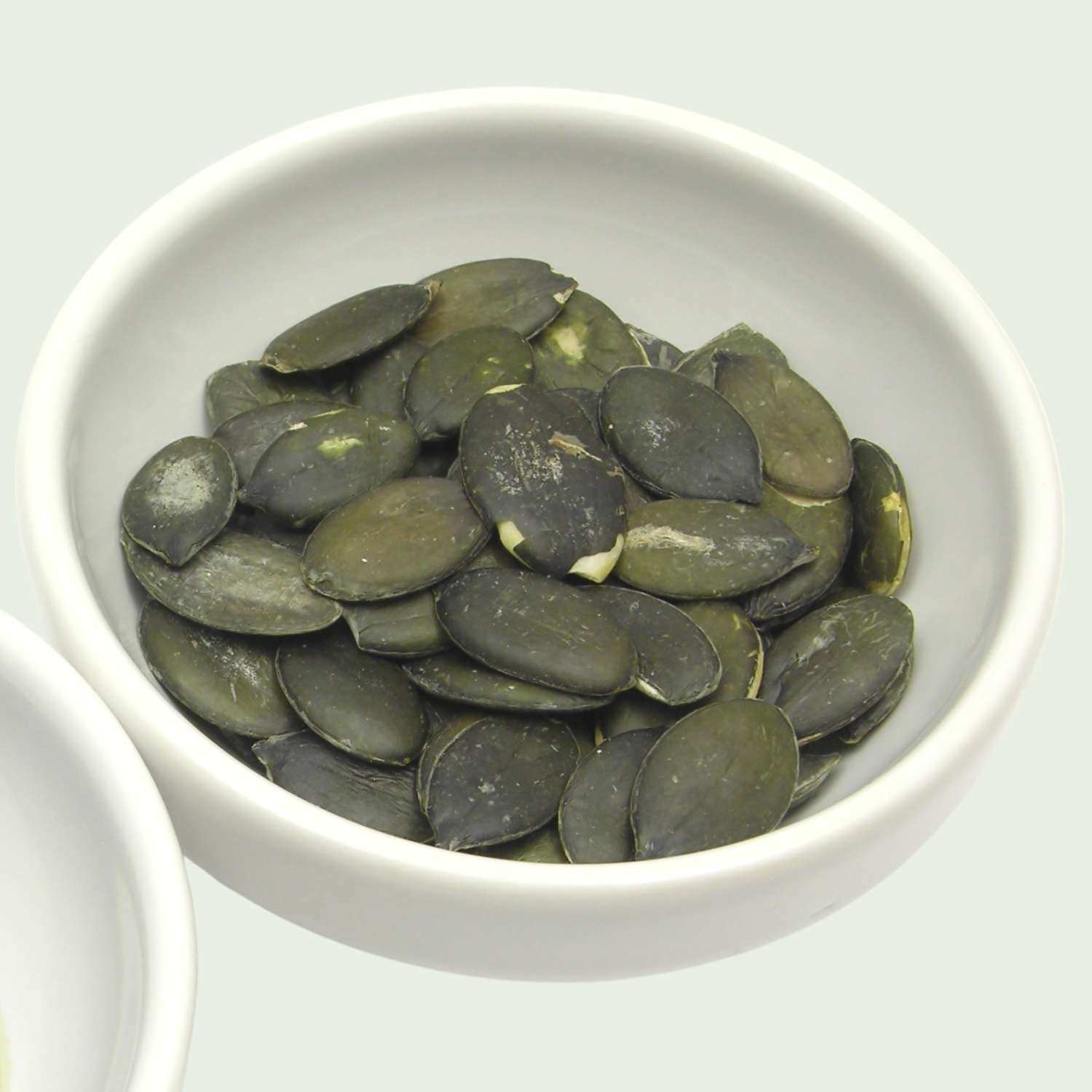 White bowl filled with dark green Australian-grown pumpkin seeds on a white background