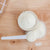 Ceramic container of white hydrolysed collagen powder with a scoop on a wooden surface.