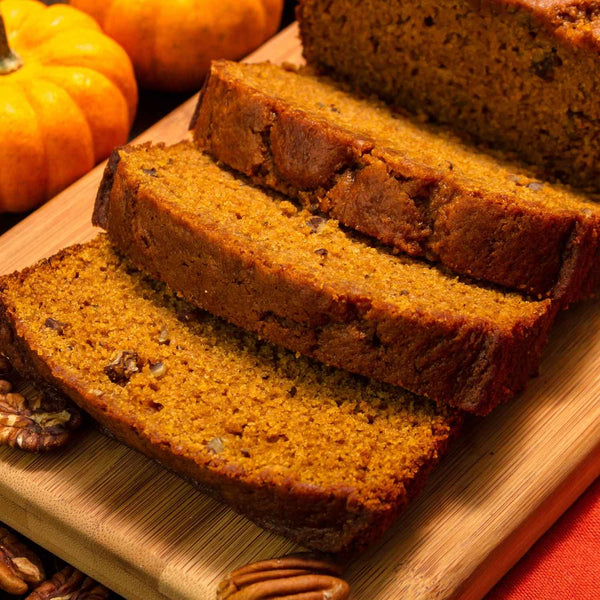 Sliced pumpkin bread made from Australian pumpkin seed meal on a wooden board with pumpkins in the background.